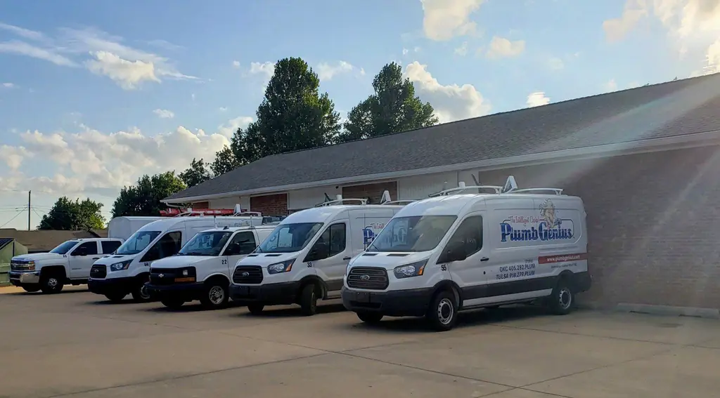 The Plumb Genius fleet parked on the apron at their Edmond shop, the nearest van's wrap showing the logo, website and phone numbers
