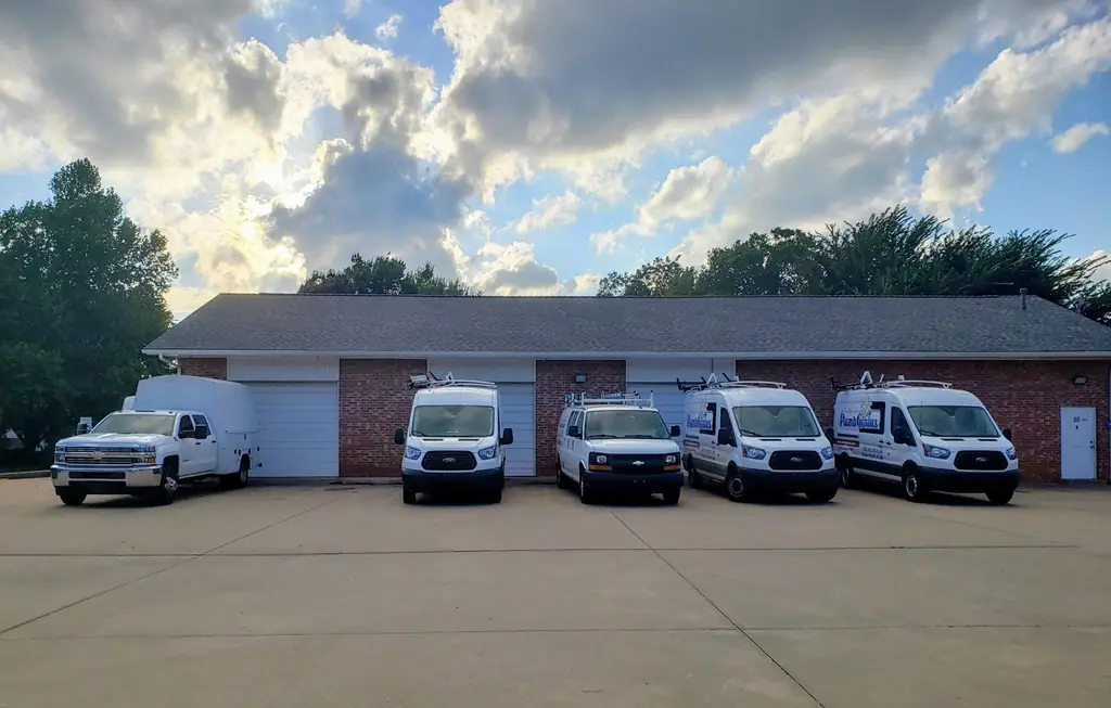 The Plumb Genius shop in Edmond at golden hour with five branded vans and a service truck lined up on the apron
